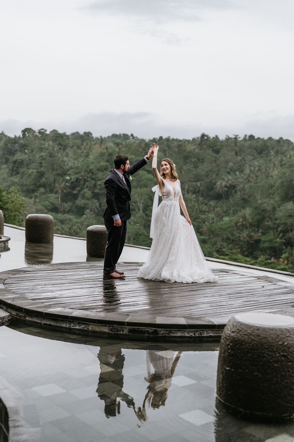 Wedding couple dancing on wet deck with mountain landscape in background.