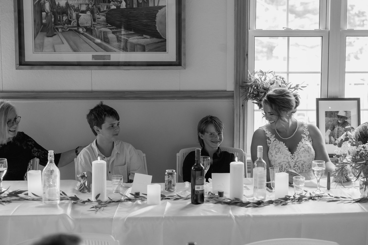A black and white photo of people seated at an elegant dining table with white tablecloth and candles.