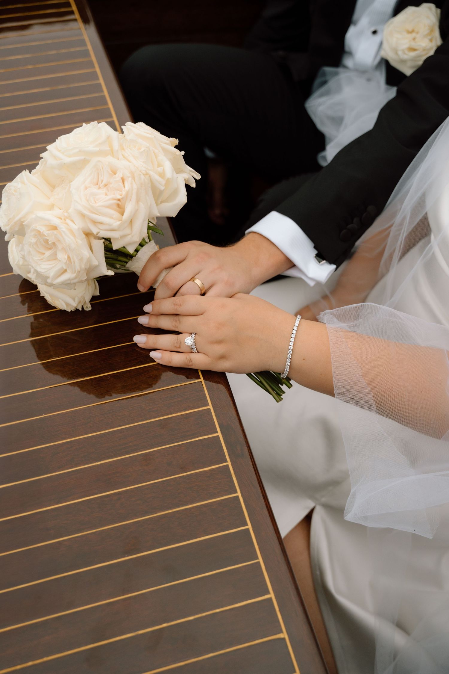 Elegant white roses bouquet and bridal hands with jewelry resting on wooden surface at wedding ceremony.
