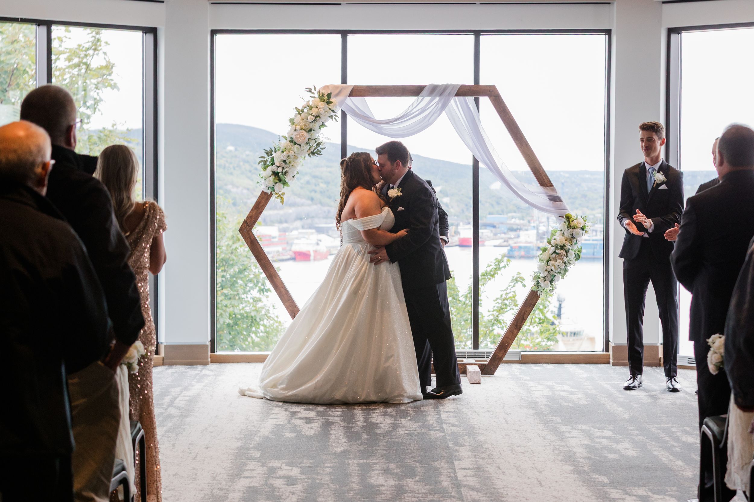 Views of a wedding ceremony in a modern venue with large windows overlooking water.