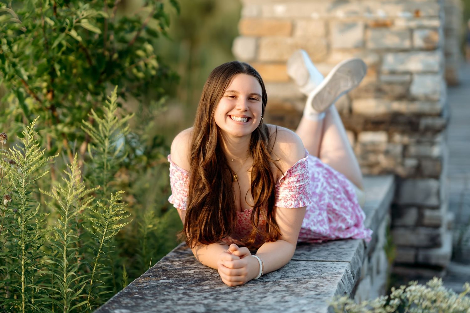 A woman in a white dress poses against a stone wall during a golden sunset photoshoot.