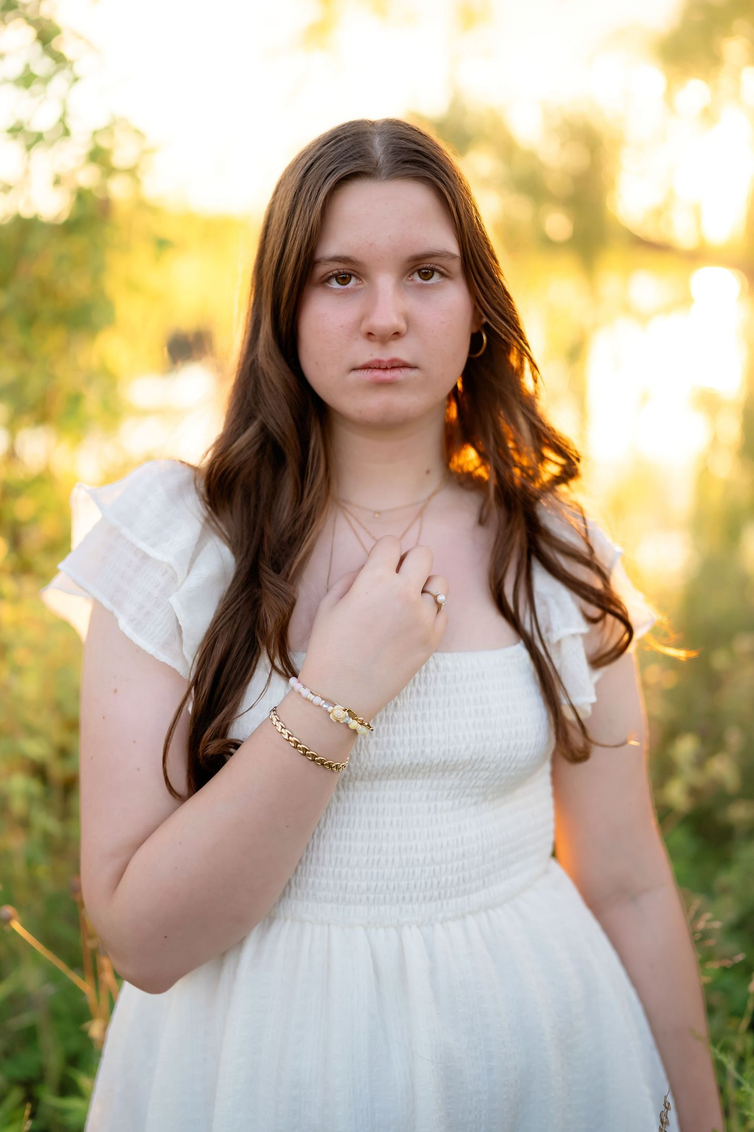 Portrait in a flowing white dress against a golden sunset bokeh background in a natural outdoor setting.