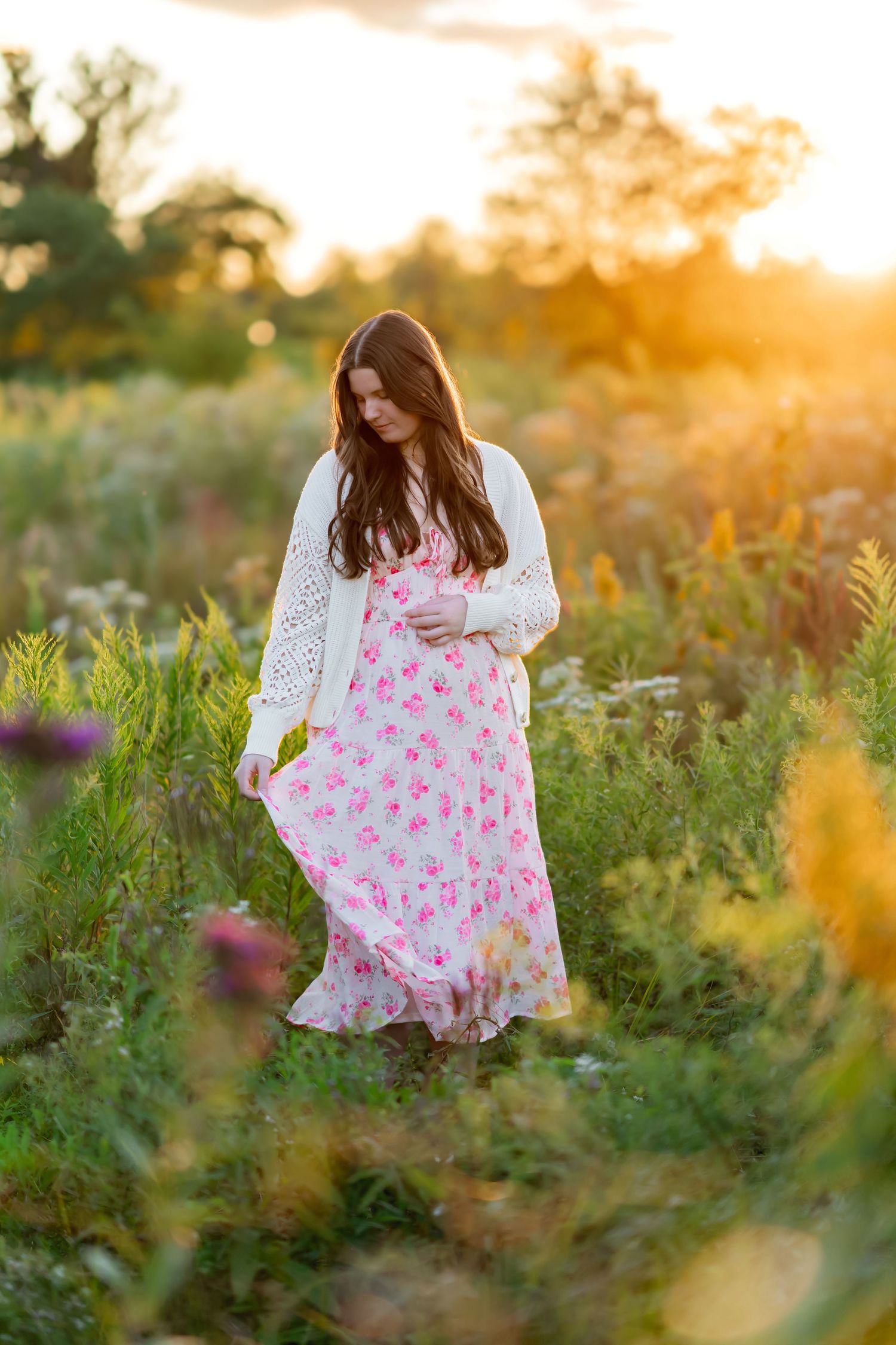 A white floral dress flows gracefully in a meadow of wildflowers during sunset.