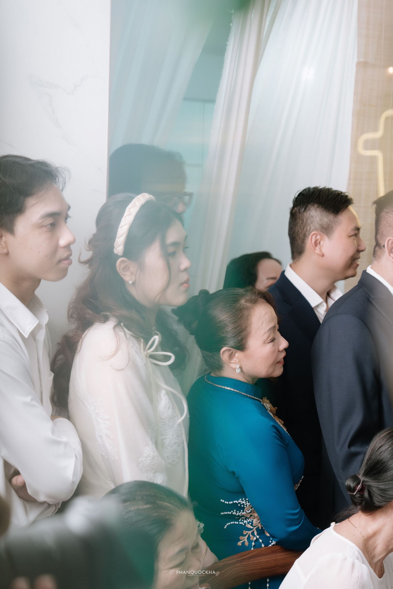 Guests in traditional Vietnamese ao dai attire observe a wedding ceremony inside a decorated church venue.