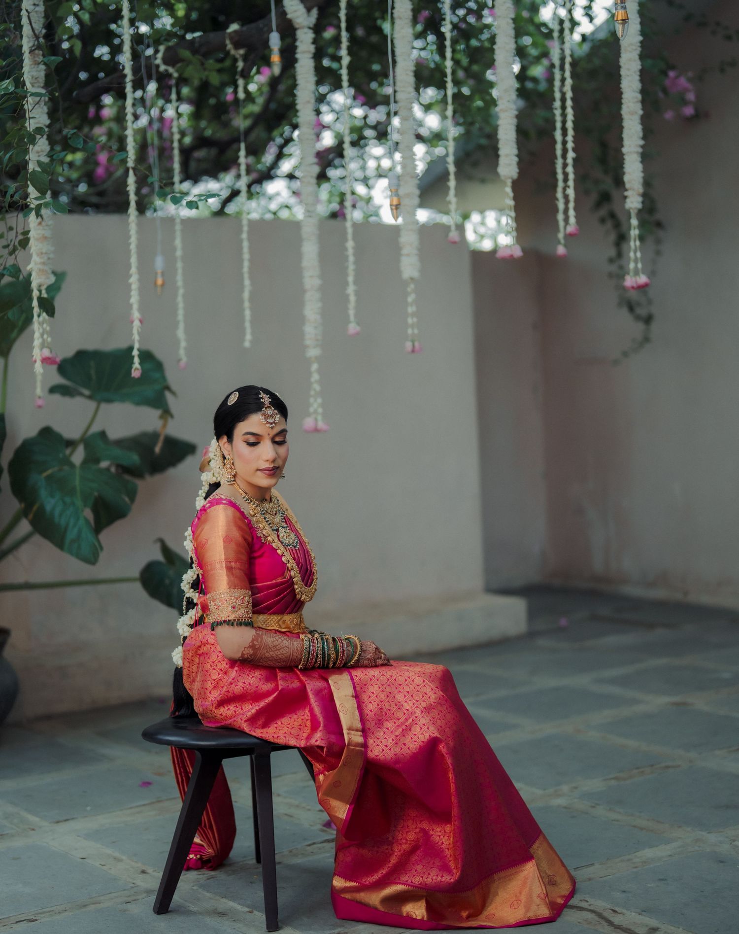 Elegant bridal pose under hanging floral decor and string lights in outdoor setting.
