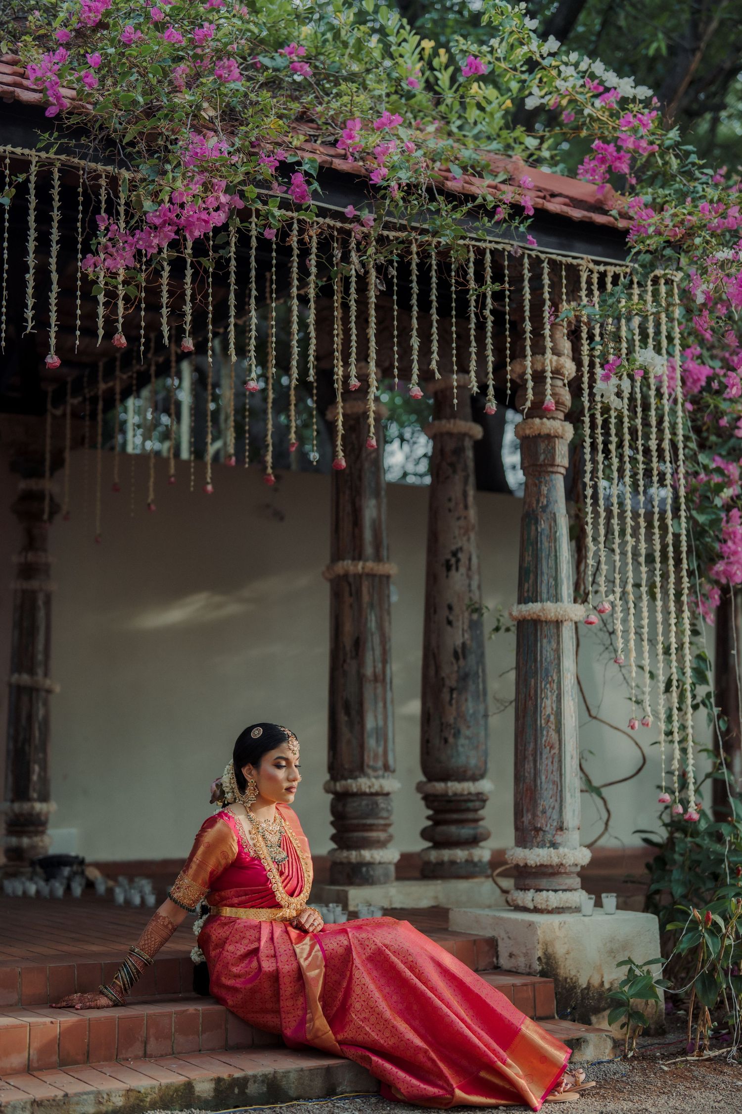 Traditional bridal portraits under a colonnade decorated with pink bougainvillea and hanging strings of lights.