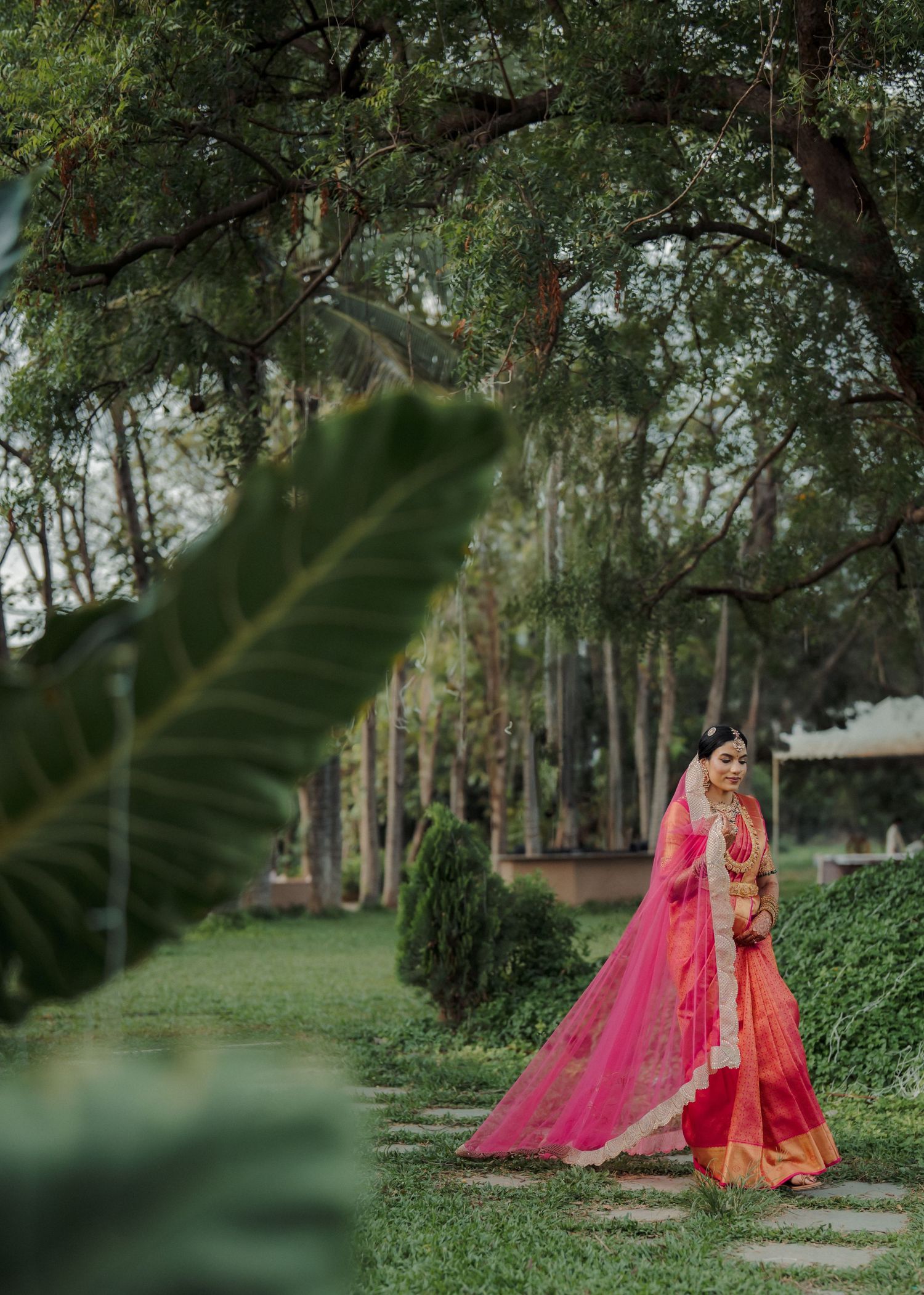 Traditional Indian bridal attire in vibrant pink and gold photographed in a lush garden setting.