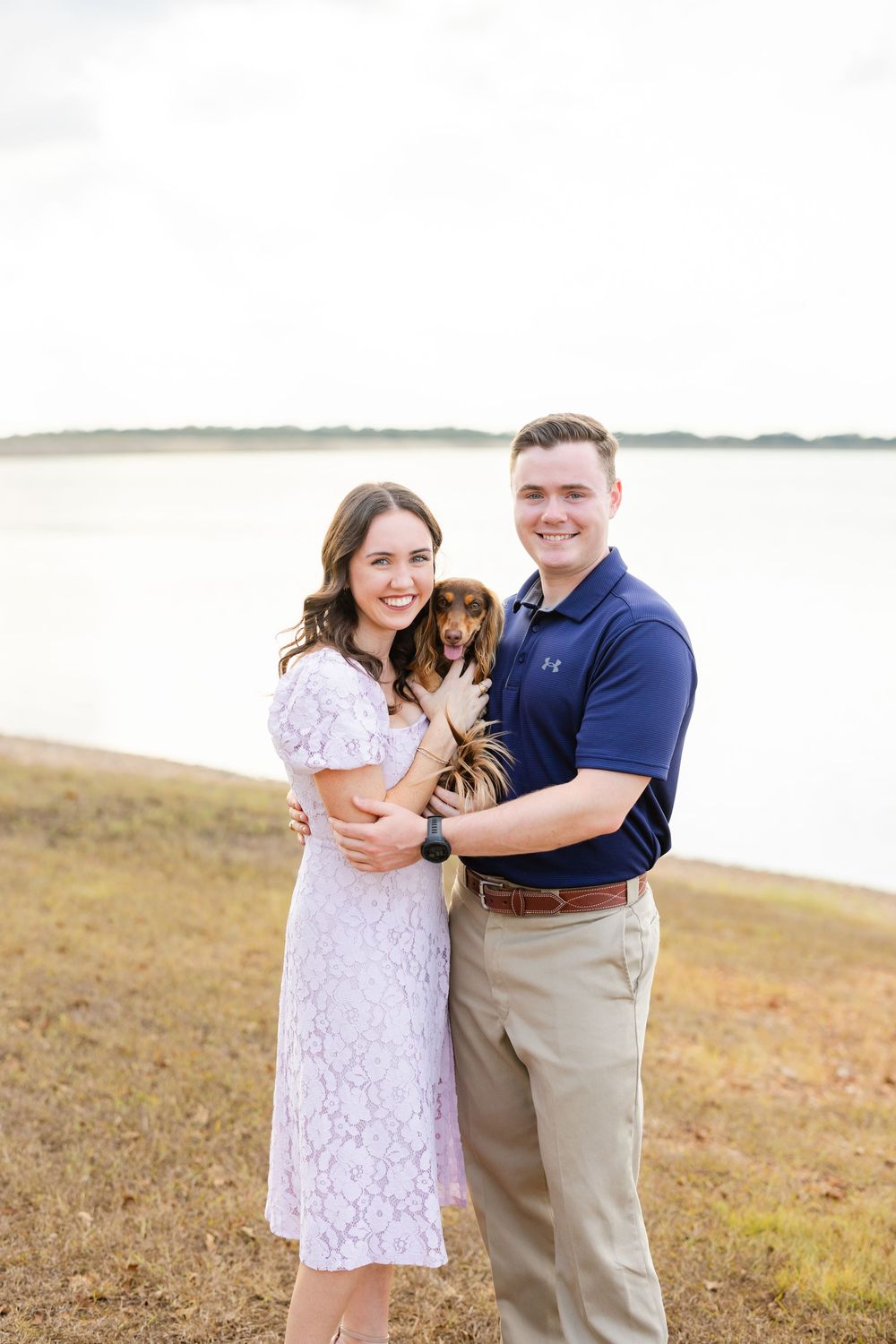 A couple embraces and smiles together on a scenic coastal meadow in matching white and navy casual attire.