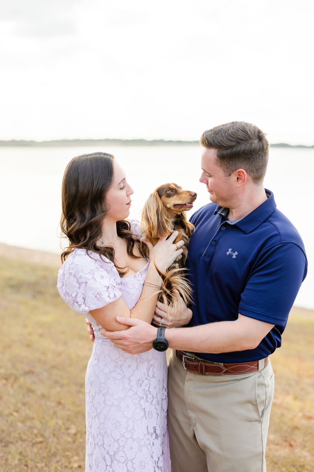 Family sharing tender moments together on a beach in casual white and blue attire during outdoor photo session.