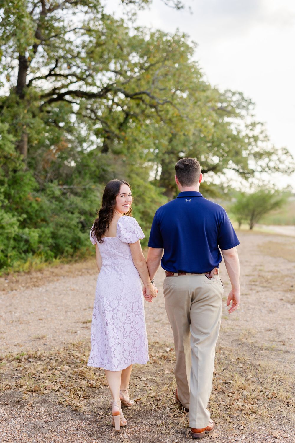 Couple walking hand in hand on a scenic dirt path bordered by trees during a sunny day.