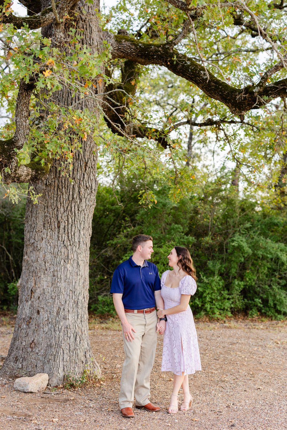 A romantic outdoor photo session with a couple standing beneath a tall oak tree on a sunny autumn day.