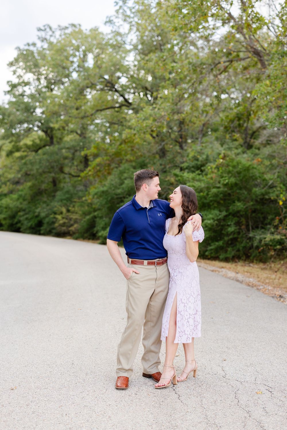 Couple shares a playful moment together on a tree-lined gravel path during a scenic outdoor photoshoot.