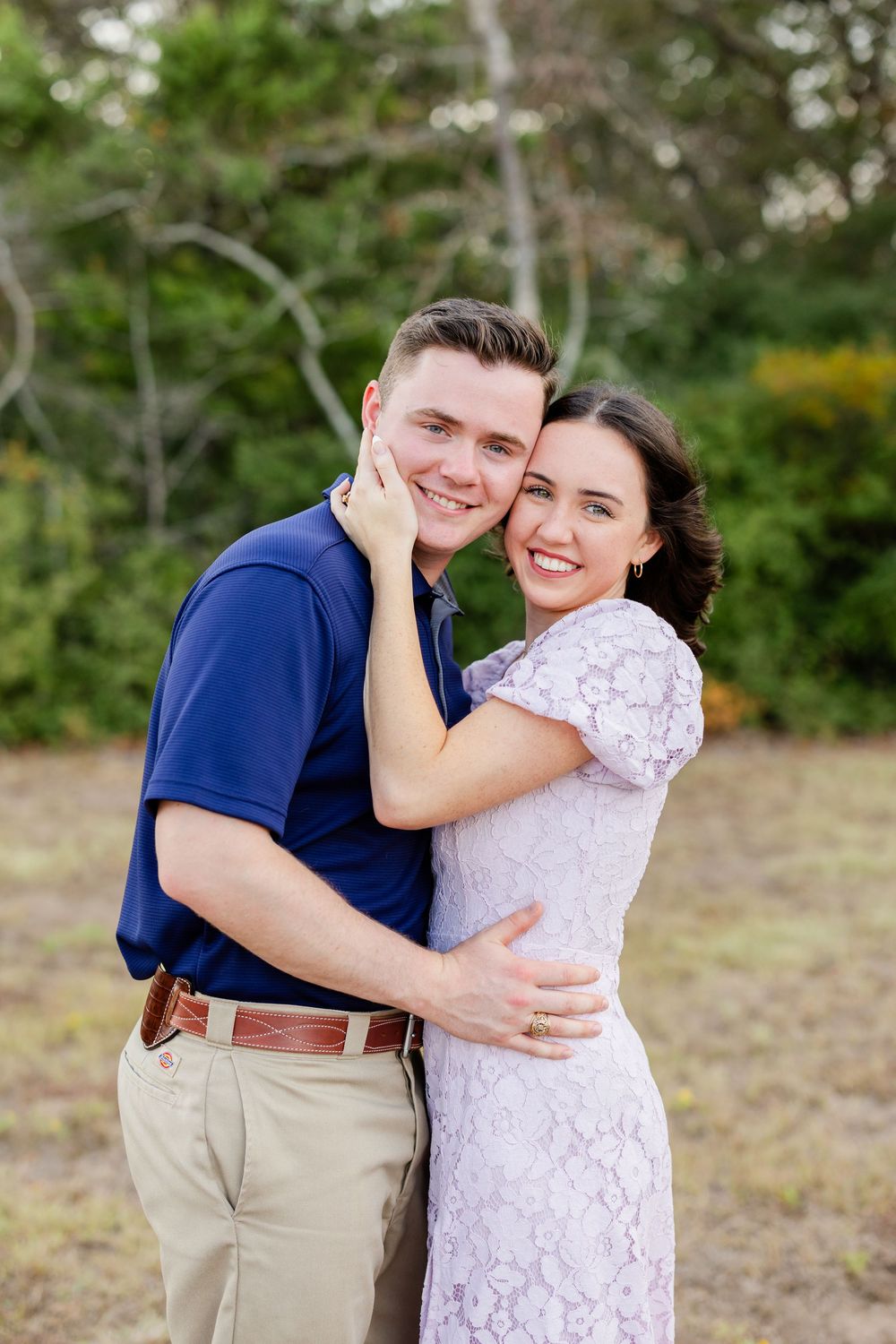 A romantic couple embraces and laughs together during an outdoor photo session in a natural setting.