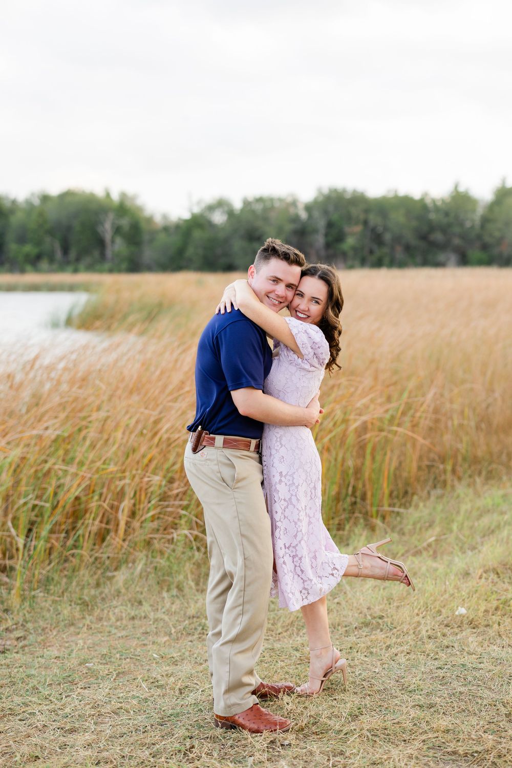 A romantic sequence of embraces in a sun-lit field of tall grass near the water.