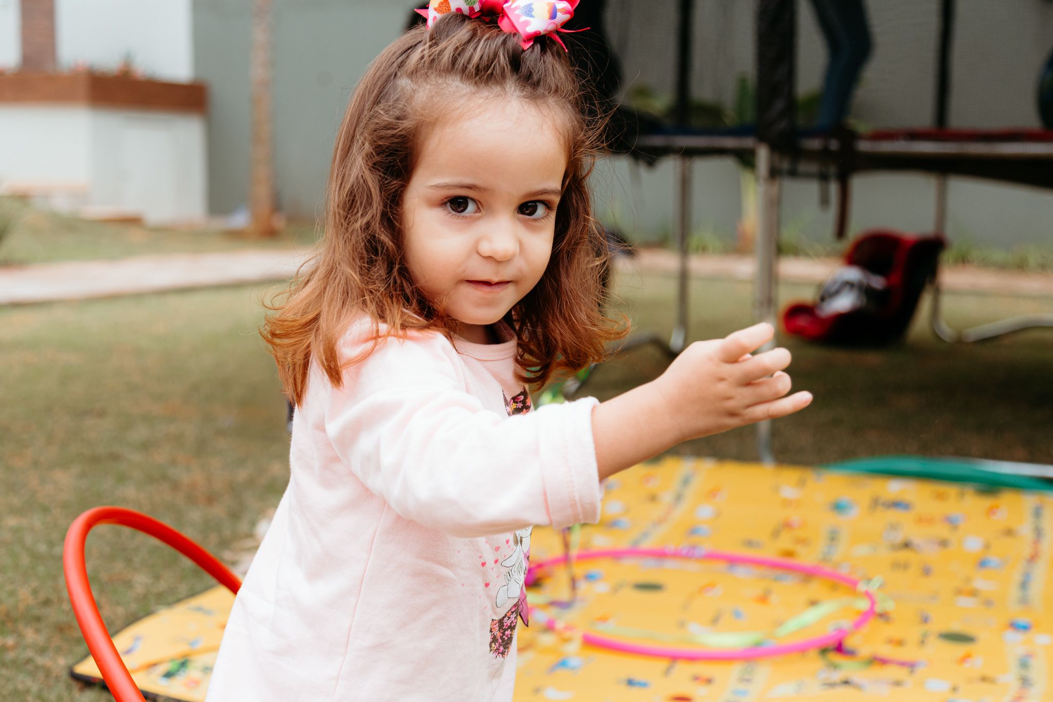 A young child in a pink dress plays with colorful books and toys on an activity mat during learning time.
