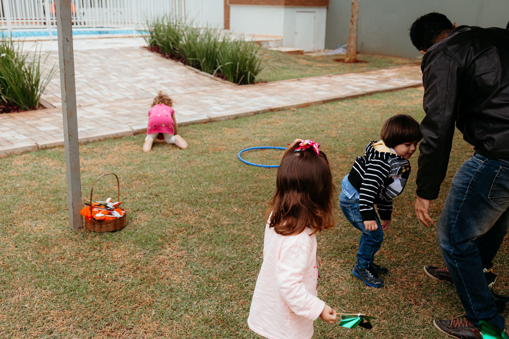 Small children participate in an outdoor Easter egg hunt on a grassy lawn with colorful plastic eggs.