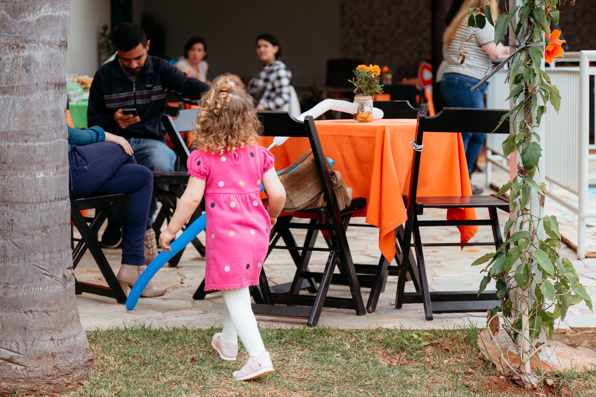 People relax at an outdoor event with orange chairs and palm trees visible in the scene.