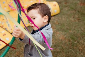 A child plays with colorful paper airplane toys in an outdoor grassy setting.