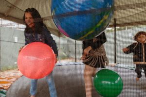 Bright colored balloons floating against a white mesh background create a festive party atmosphere indoors.