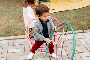 Young child playing with colorful hula hoops on a paved patio during outdoor activities.