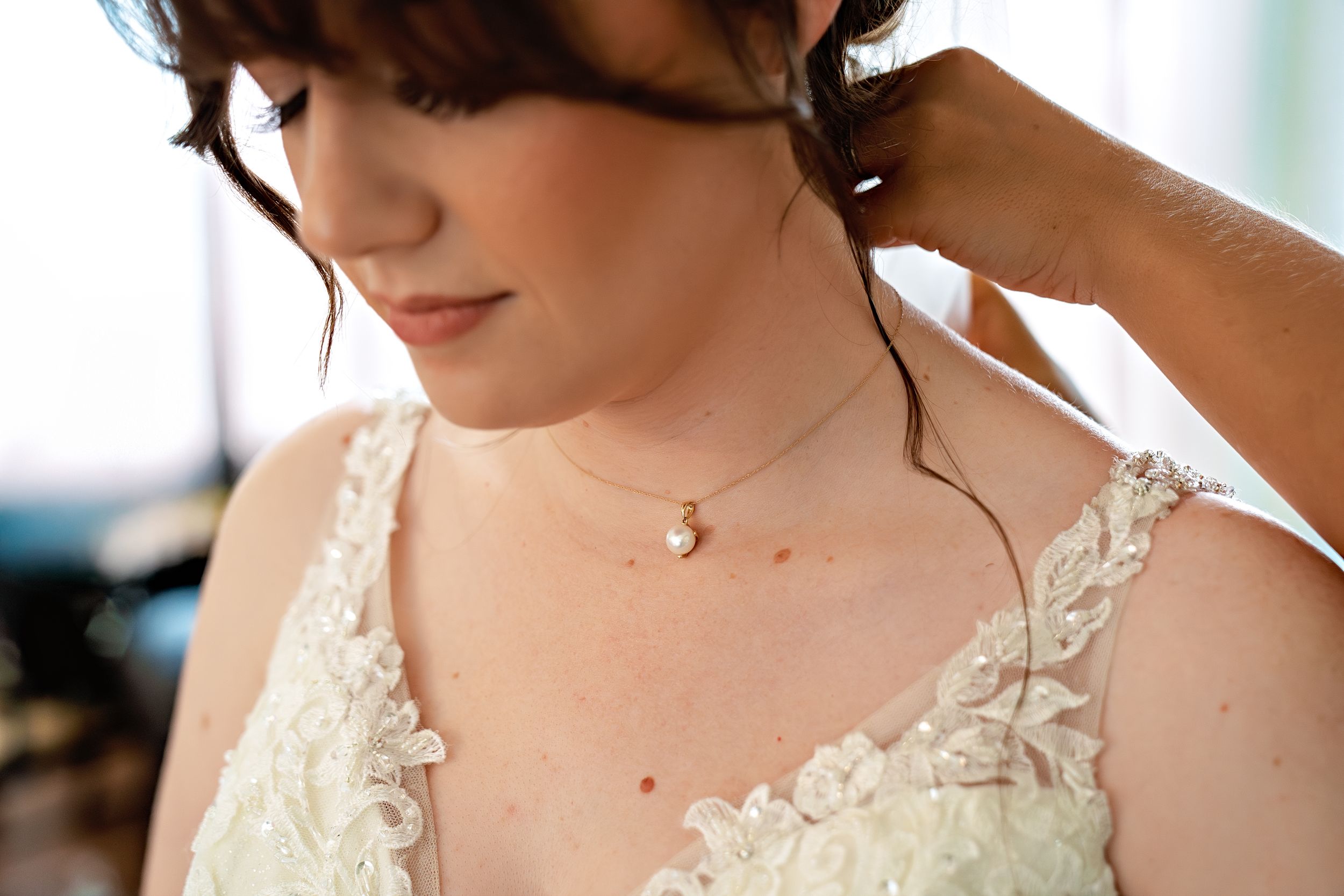 A close-up shot of delicate lace details on a white wedding dress with a dainty necklace pendant.