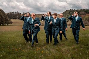 Wedding party in blue dresses and suits joyfully running through an open meadow under dramatic cloudy skies.