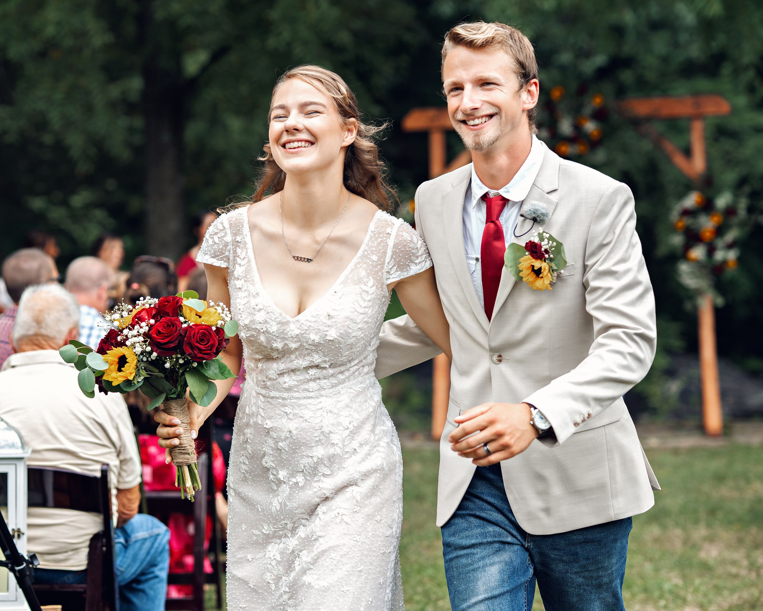 Two newlyweds walk hand in hand outdoors and share joyful laughter during their rustic countryside wedding celebration.