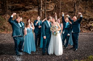 Wedding party in blue and white attire poses together on rustic outdoor stone backdrop for group photos.