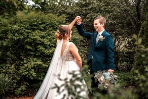 Wedding party celebrates outdoors in a garden setting with joyful dance moves.