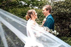 Wedding party members in navy suits and pink ties share a candid moment together outdoors near greenery.