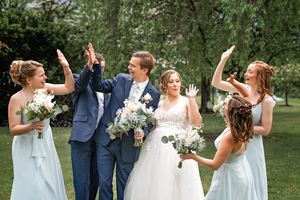 Bridal party in blue dresses and navy suits dances together on green lawn.