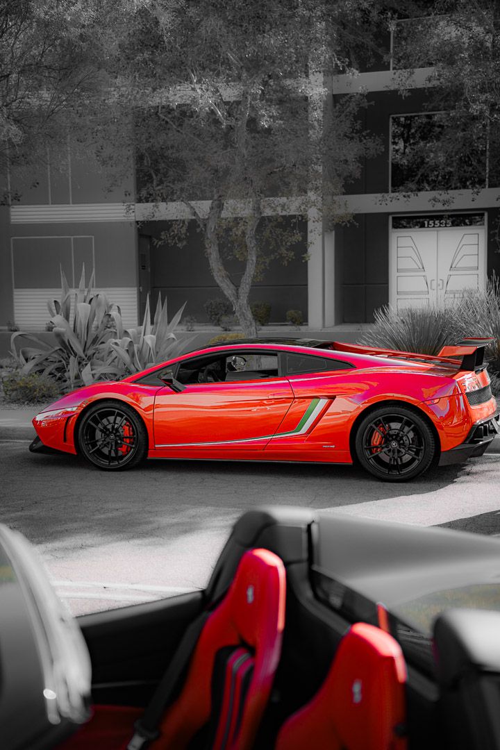 A striking red Lamborghini Gallardo supercar parked in front of a modern building with black wheels and aerodynamic bodywork.