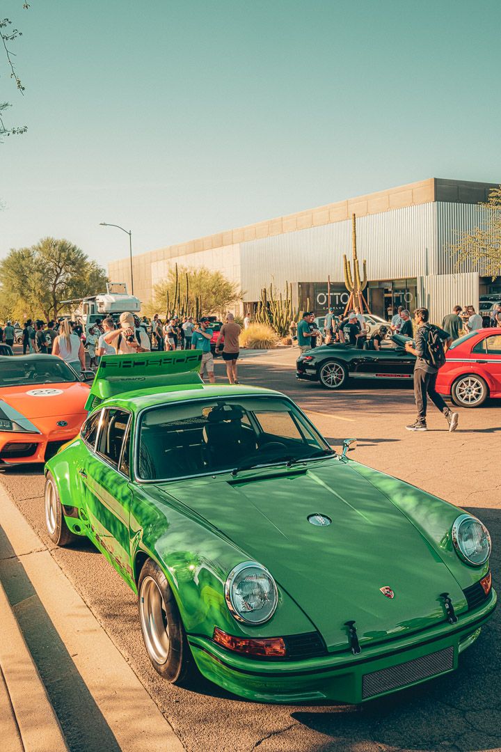 Bright green vintage Porsche 911 on display at an outdoor car meet with desert scenery in the background.