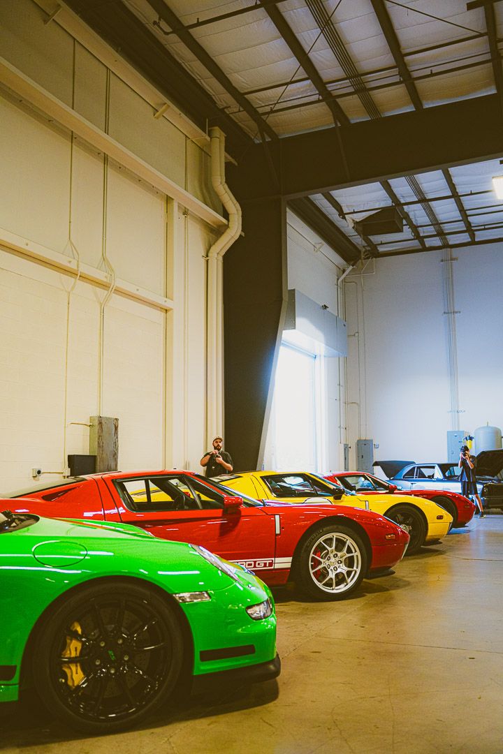 Colorful lineup of Porsche sports cars including green, red, and yellow models in warehouse display.