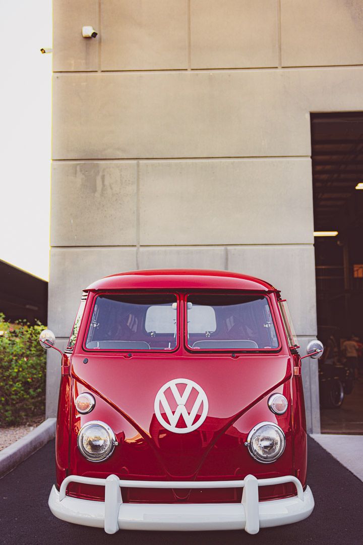 A classic red Volkswagen bus with white trim and iconic VW logo viewed from the front.