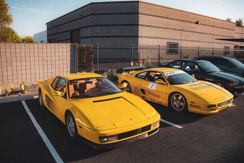 Yellow Ferrari Testarossa sports cars lined up in a parking lot with modern buildings in the background.
