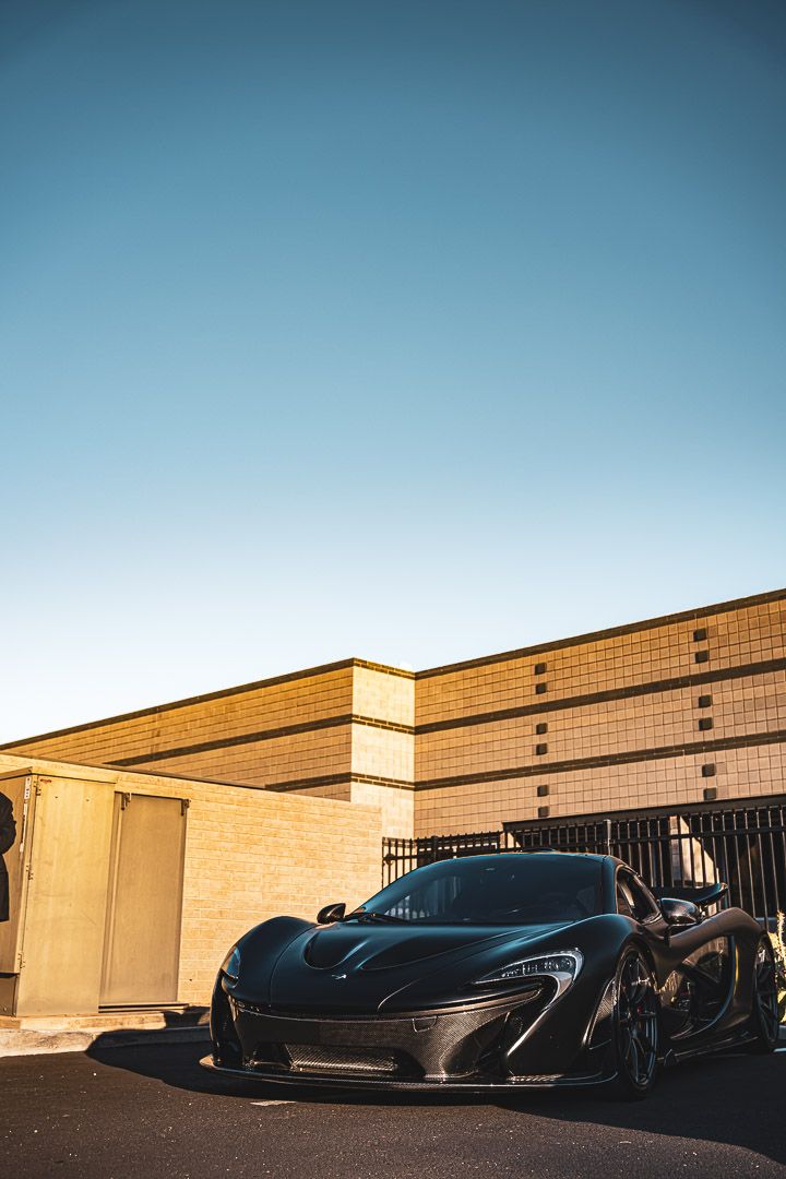 Multiple black luxury supercars parked in a row outside a brick building at sunset.