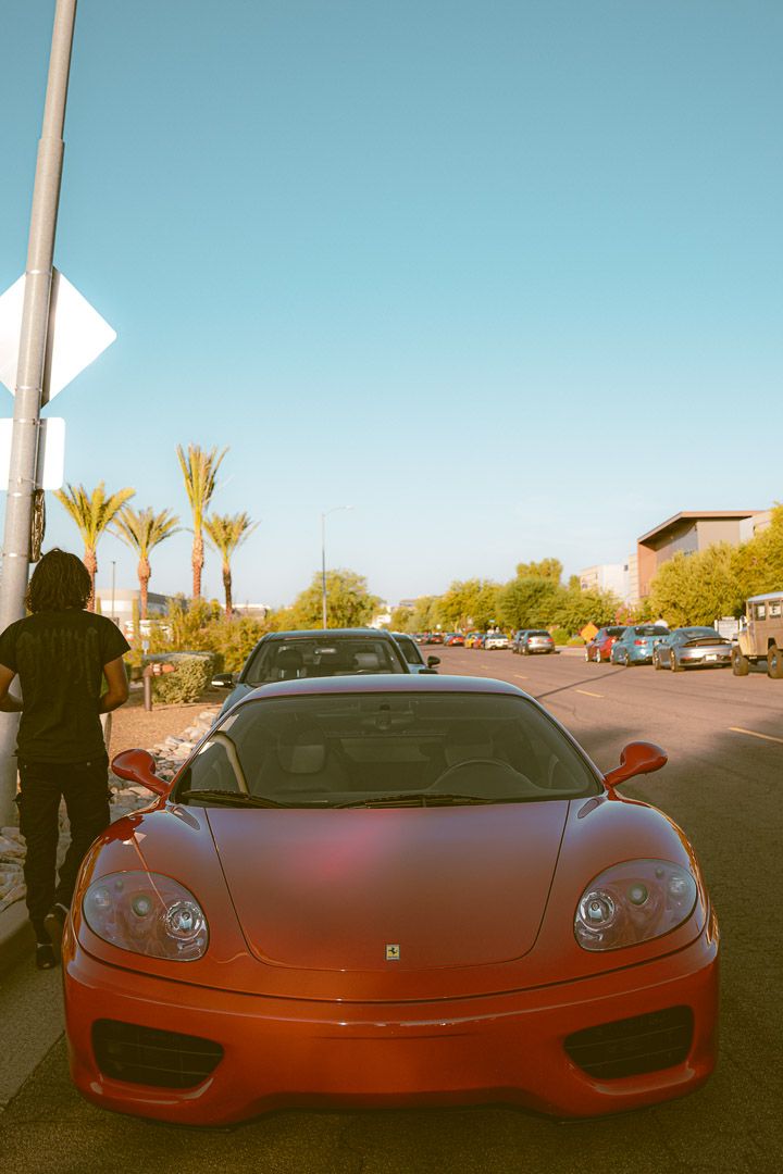 Red Ferrari sports car parked in a sunny lot with palm trees in the background.