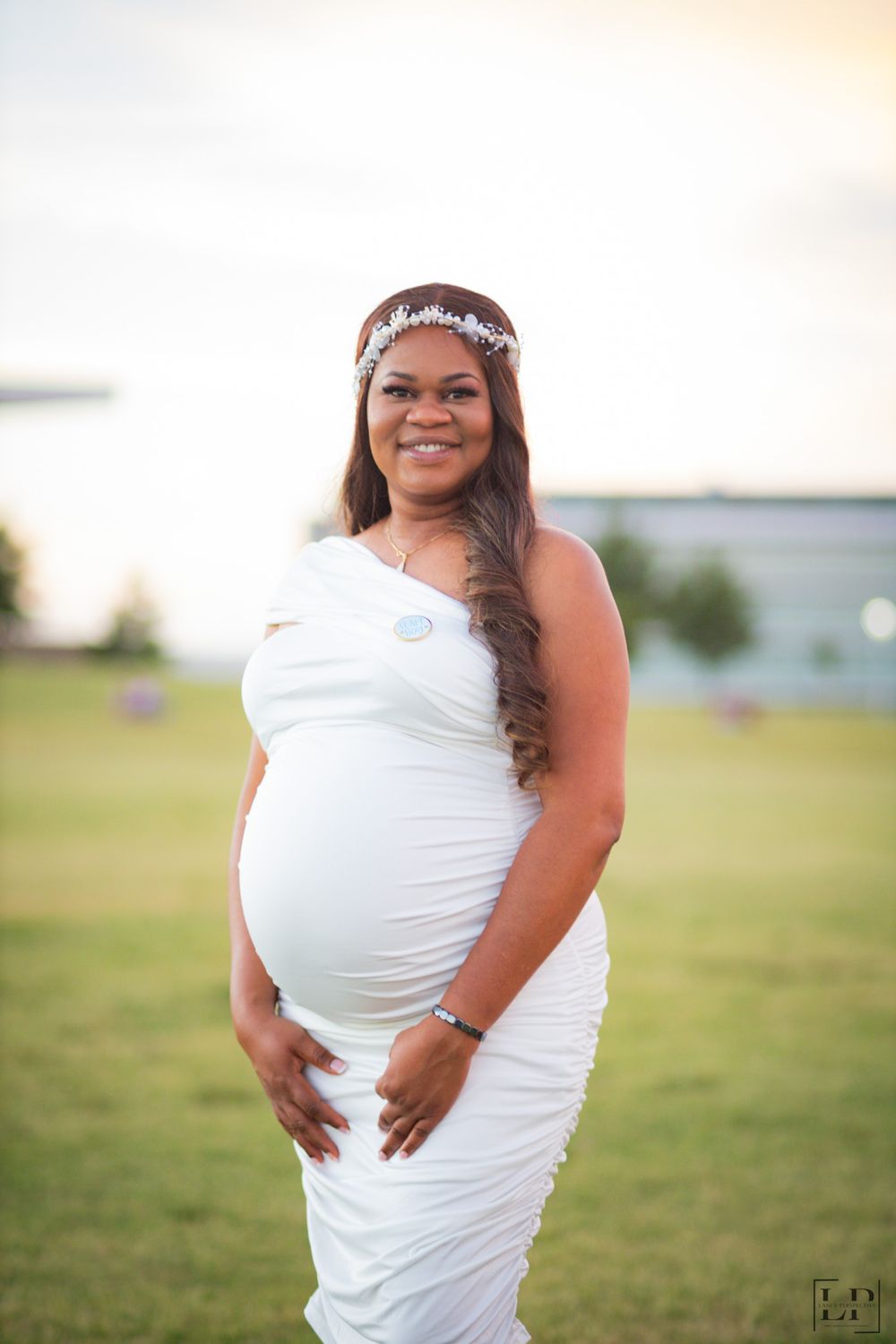 Joyful maternity photos captured outdoors with a white dress and decorative headpiece.
