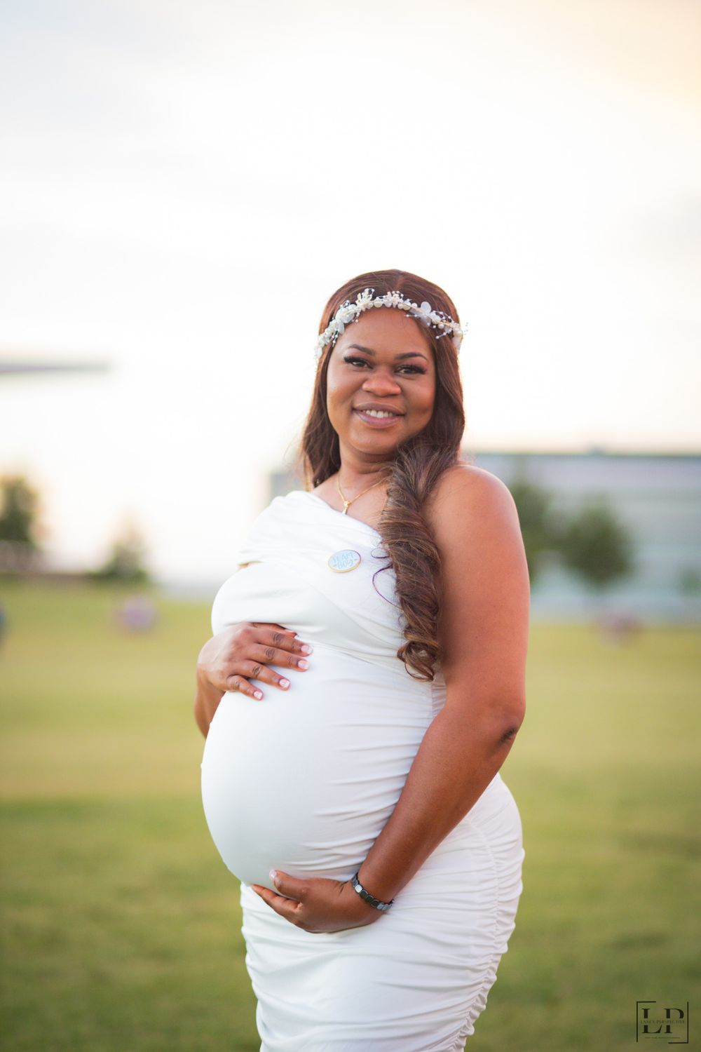 Outdoor maternity portraits featuring a white dress and delicate headpiece in warm evening light.