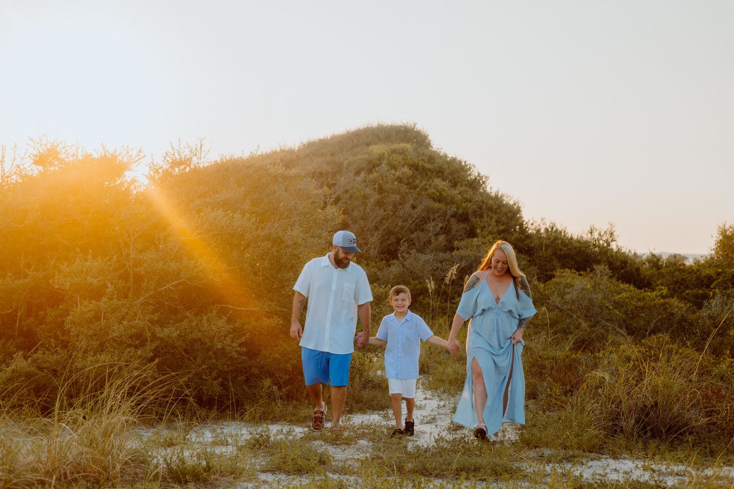 Family walking together on beach path during golden sunset.