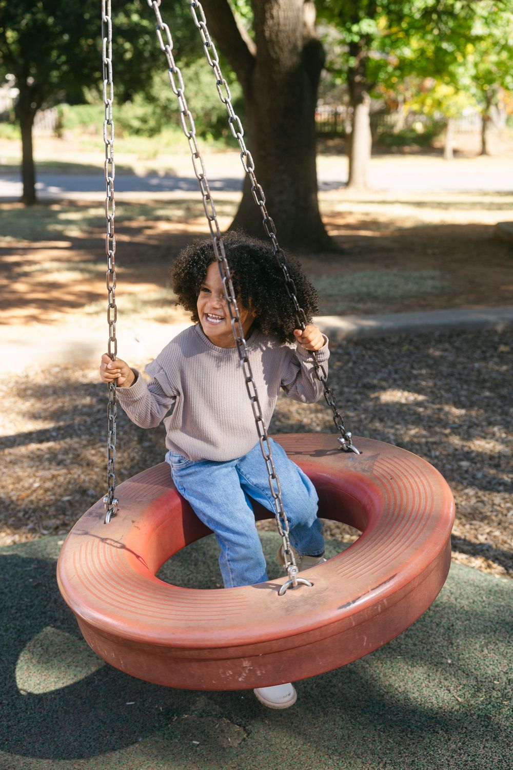 A person enjoys swinging on a large circular tire swing in a peaceful outdoor park setting.