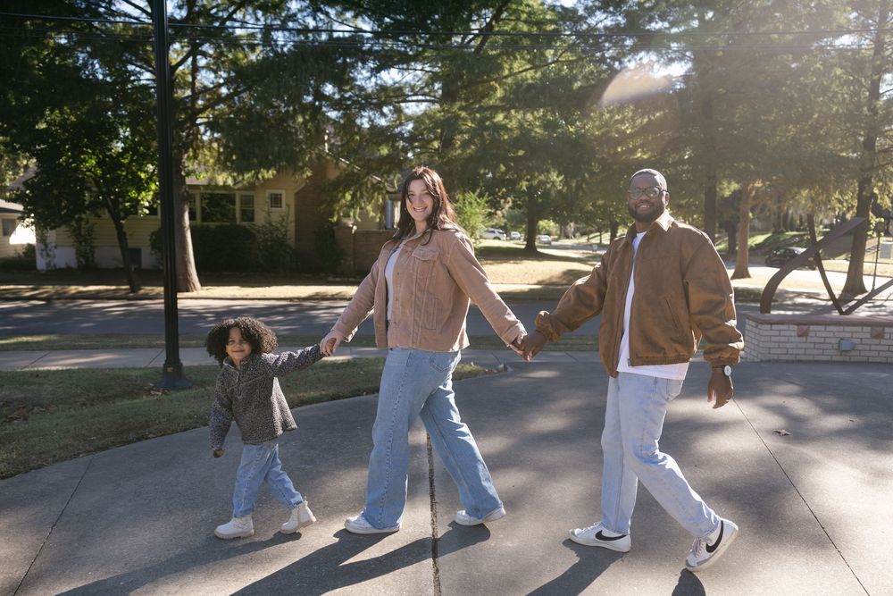 A group of people walking in a line on a sunny sidewalk casting long shadows on the pavement.