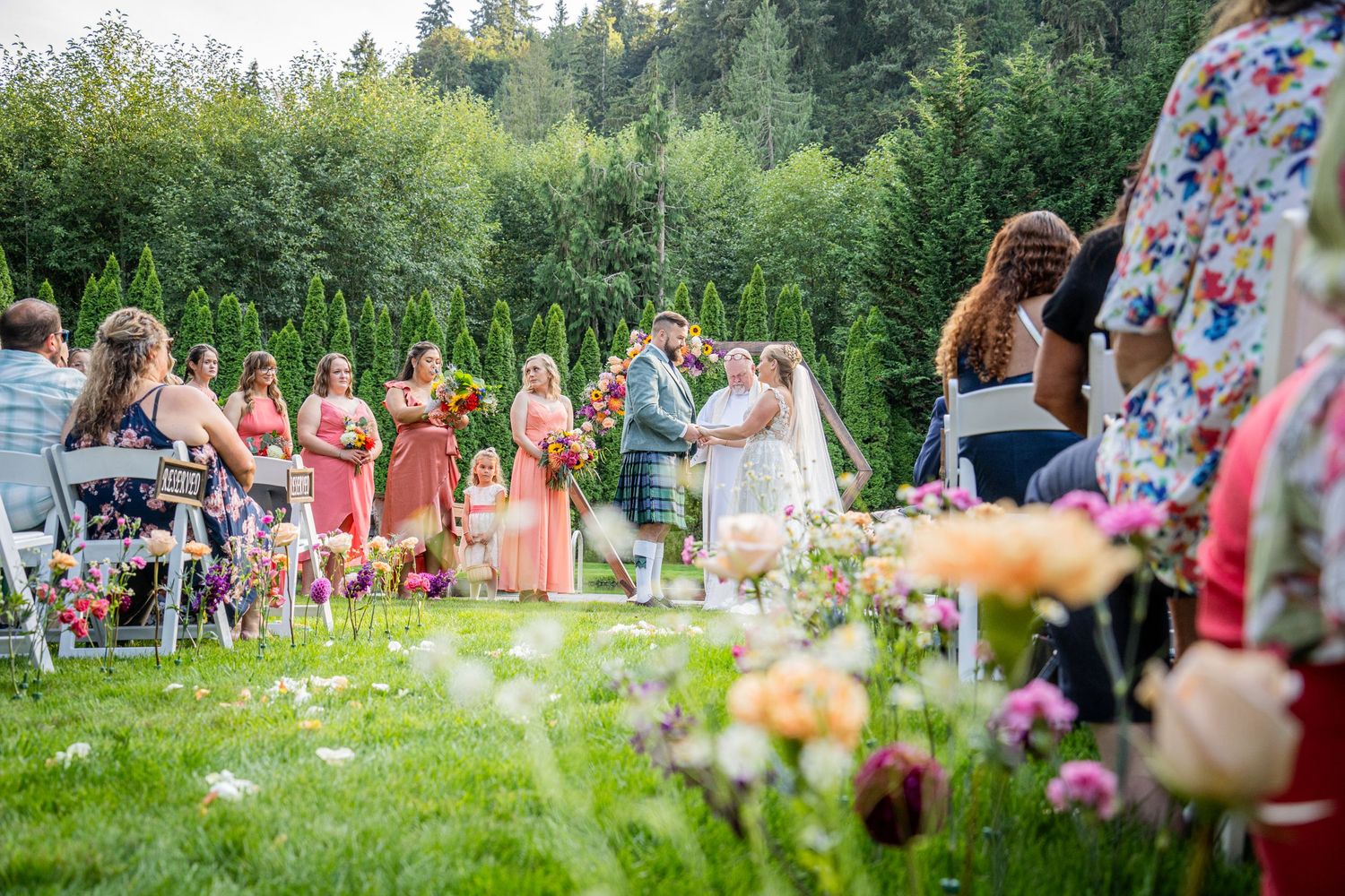 Wedding ceremony in a landscaped garden with coral bridesmaid dresses and floral decorations.