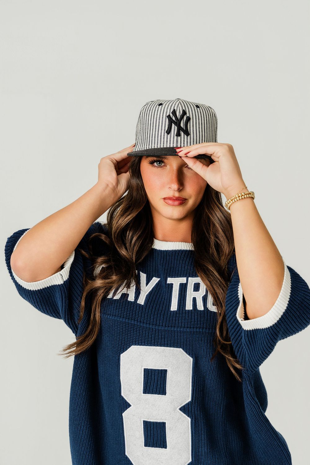 A series of photos showing someone adjusting a Yankees baseball cap while wearing a navy blue sweater.
