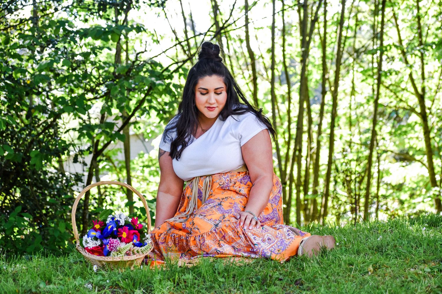 Portrait of a woman in an orange dress standing between two mossy trees in a forest, with dappled light on the ground. Kent, WA.