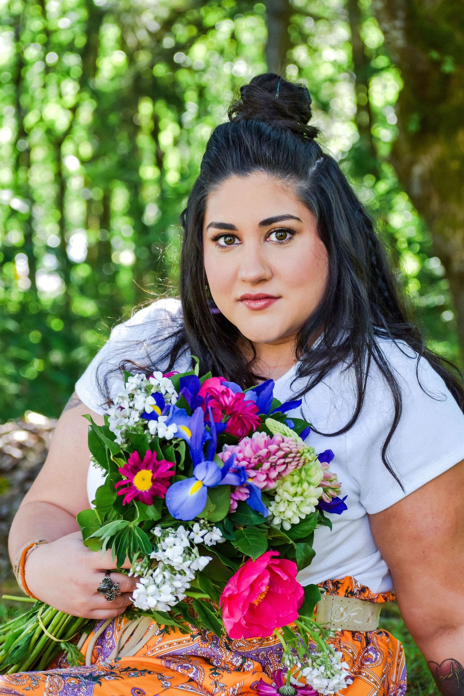 Portrait of a woman in an orange dress standing between two mossy trees in a forest, with dappled light on the ground. Seattle, WA