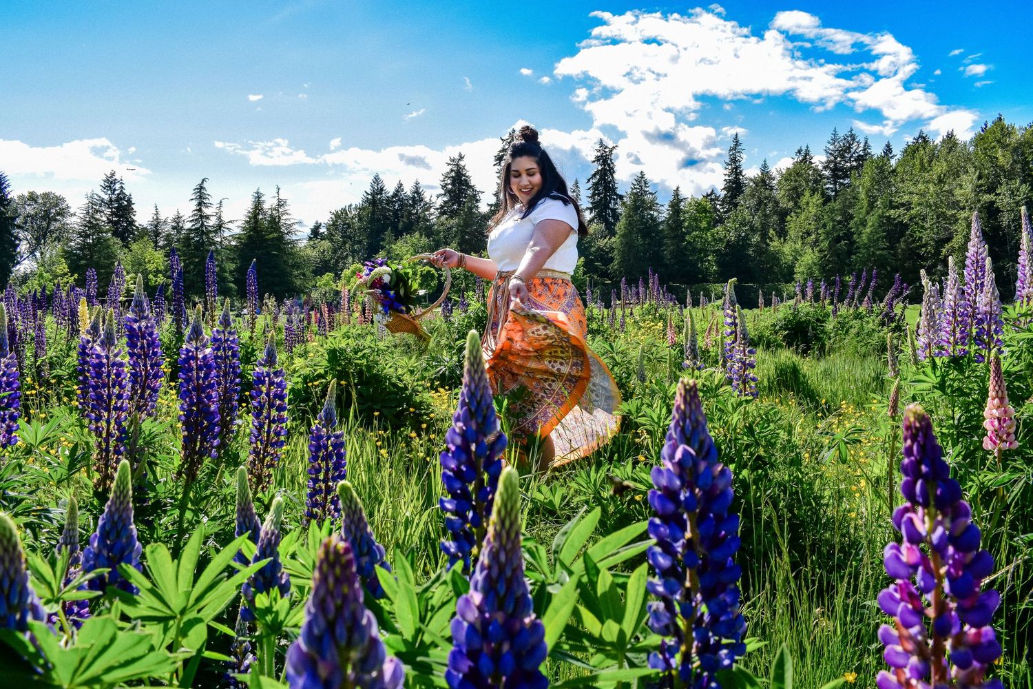 Stylish woman in a flower field wearing sunglasses and a white top, surrounded by tall purple lupines and blue skies. Lupin Session. Seattle