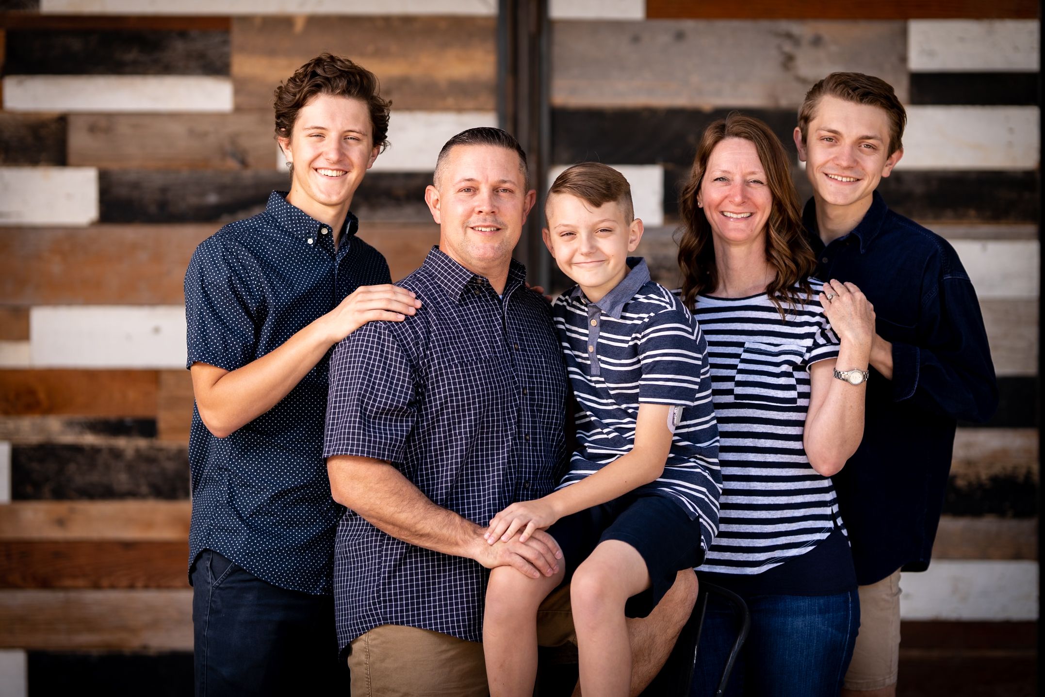 Casual family portrait with wooden plank wall backdrop.
