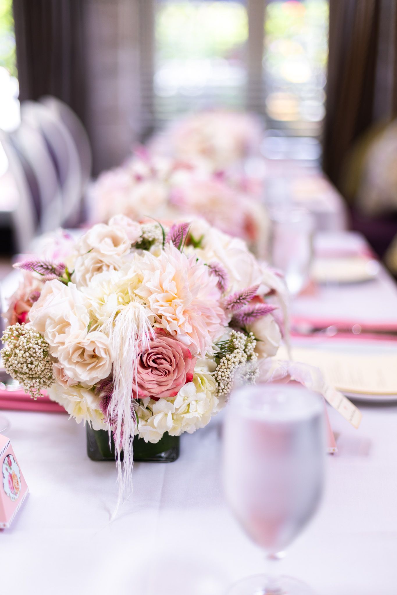 Elegant pink and white floral centerpiece with roses and feathers on formal dining table.